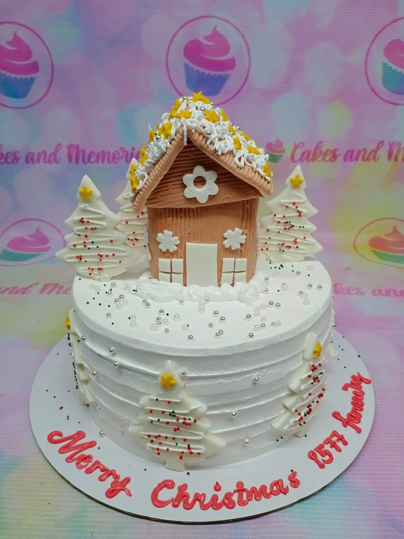 White soft-icing Christmas cake featuring a gingerbread house topper and white chocolate Christmas trees with silver dragees.
