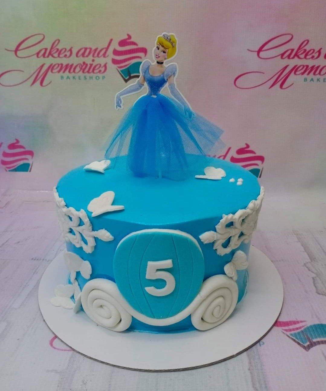 Blue Cinderella themed birthday cake with a character topper, white carriage design, and butterfly accents.