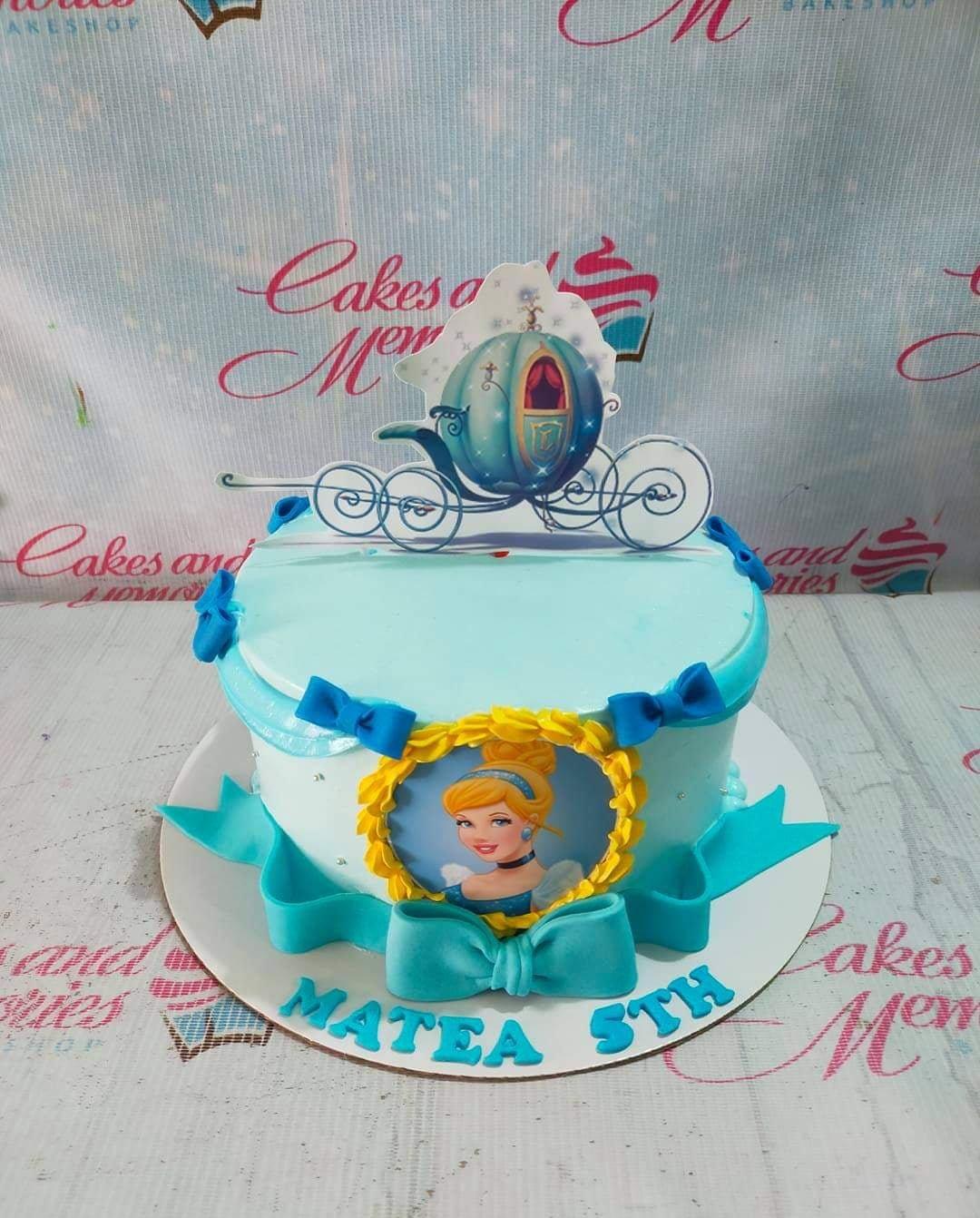 Light blue Cinderella themed cake with a carriage topper, Cinderella portrait, and blue fondant bows.