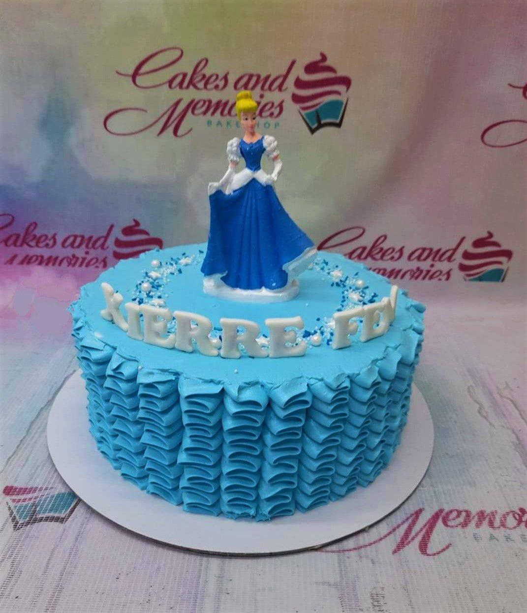 Light blue 1-tier Cinderella themed cake with vertical icing ruffles and a Cinderella figurine topper.