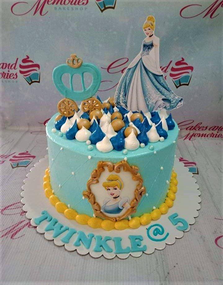 Light blue Cinderella themed birthday cake with a large character printout, a carriage topper, and blue and white icing dollops.