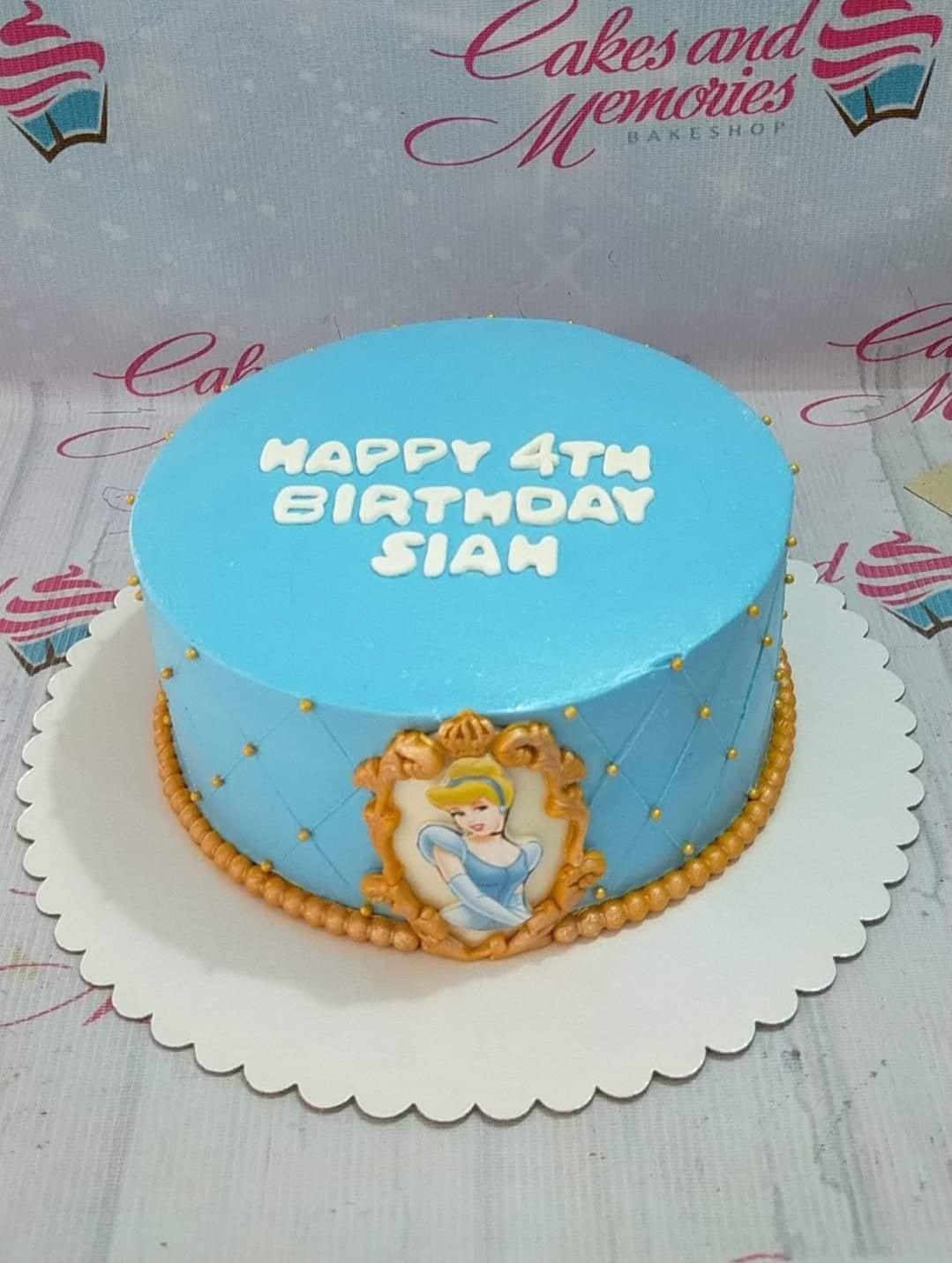 Light blue Cinderella themed birthday cake with quilted icing pattern, gold dragees, and a Cinderella printout in a gold frame.