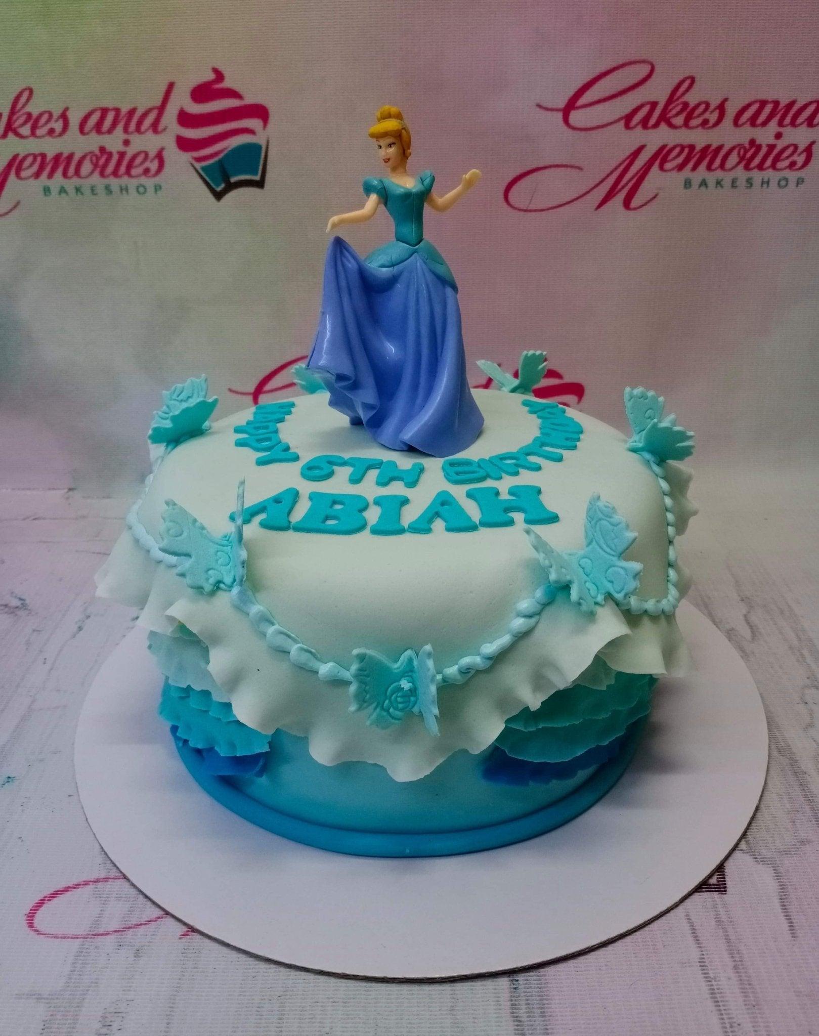 Cinderella themed blue ombre ruffle cake with a princess figurine and butterfly decorations.