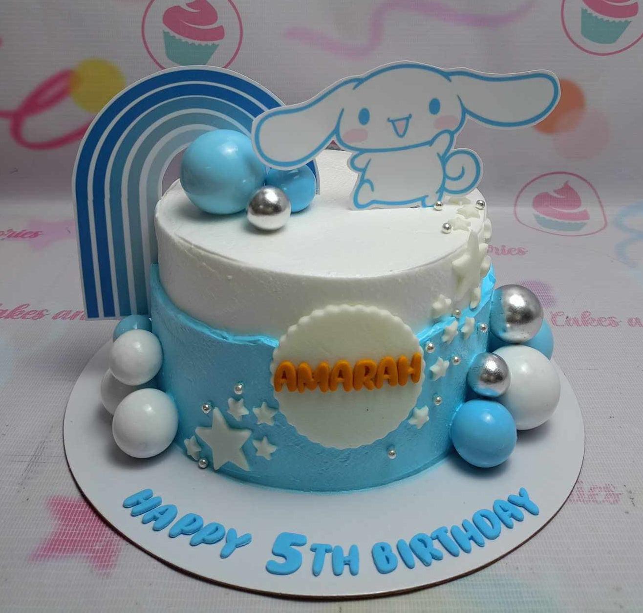 White and light blue Cinnamoroll themed birthday cake with a rainbow topper, plastic balls, and stars.
