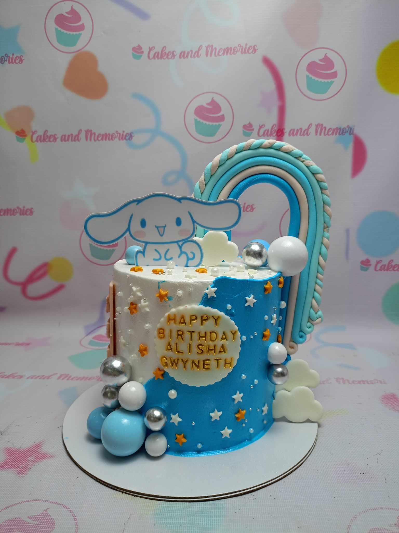 Cinnamoroll themed birthday cake with blue and white icing, a large rainbow topper, and white and silver spheres.