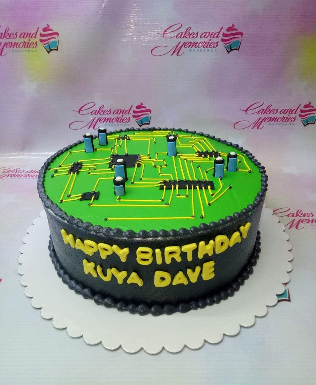 Circuit board themed birthday cake with black icing, green top, and yellow piped circuit lines and electronic components.