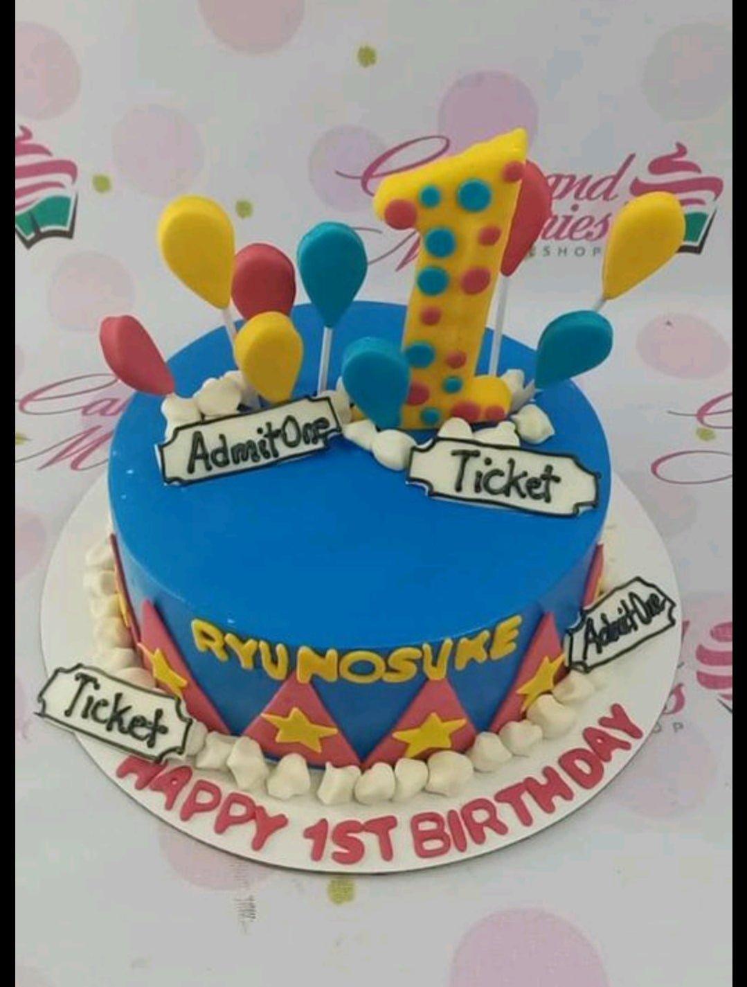 Circus themed 1st birthday cake in blue with yellow number one topper, balloons, and ticket decorations.