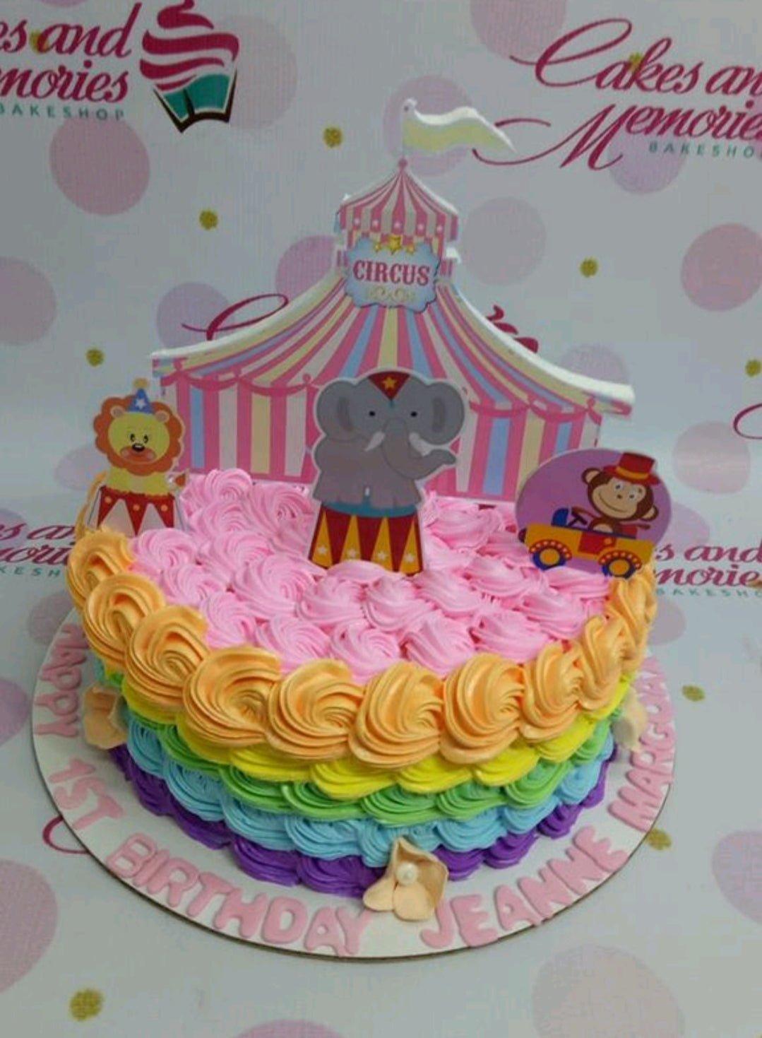 Rainbow circus themed birthday cake with pink, orange, yellow, green, blue, and purple icing ruffles and animal printout toppers.
