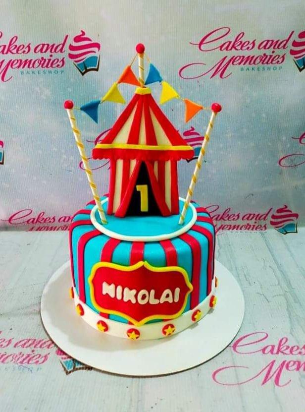 Circus themed 1-tier fondant cake with red and blue stripes, a 3D circus tent topper, and the name Nikolai on a red plaque.