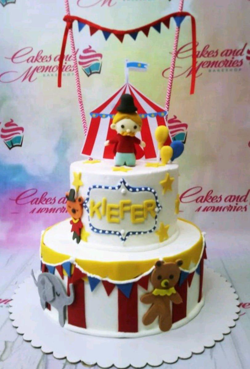 Two-tier circus-themed fondant cake in red, white, and yellow with a ringmaster topper and animal decorations.
