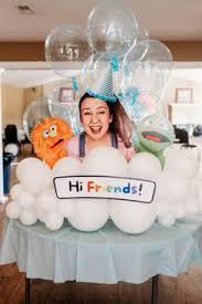 A whimsical white cloud-themed cake featuring a central character and puppets with a 'Hi Friends!' message.