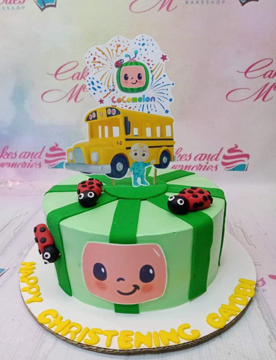 Light green Cocomelon themed cake with dark green stripes, ladybug toppers, and a yellow school bus printout.