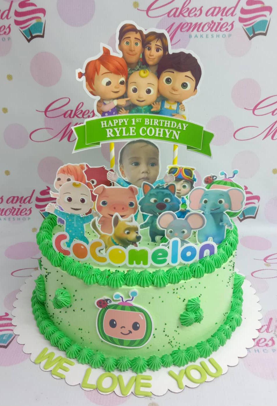 Light green Cocomelon birthday cake with character printouts, green icing rosettes, and a personalized photo topper.