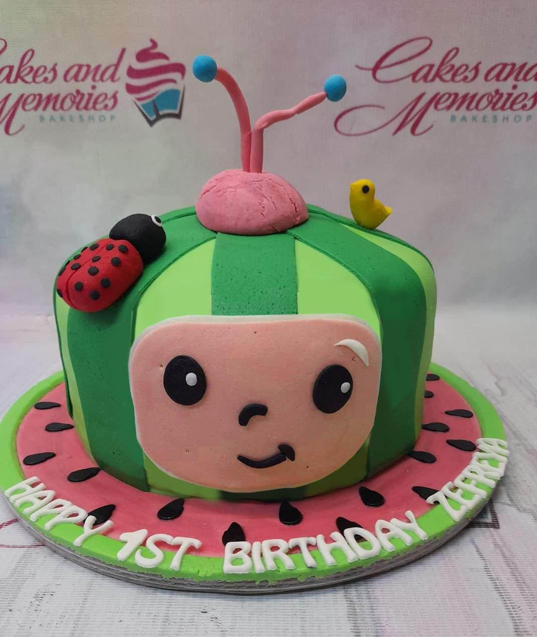 Cocomelon themed watermelon cake with a 3D character face, ladybug, and bird toppers on a pink watermelon slice base.