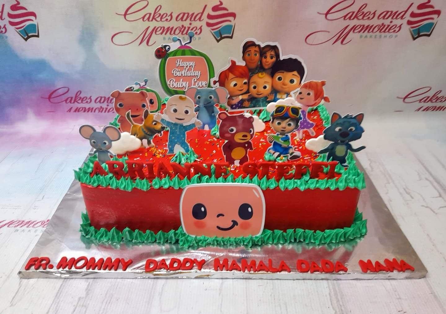 Red rectangular Cocomelon birthday cake with green icing grass borders and various character printouts.