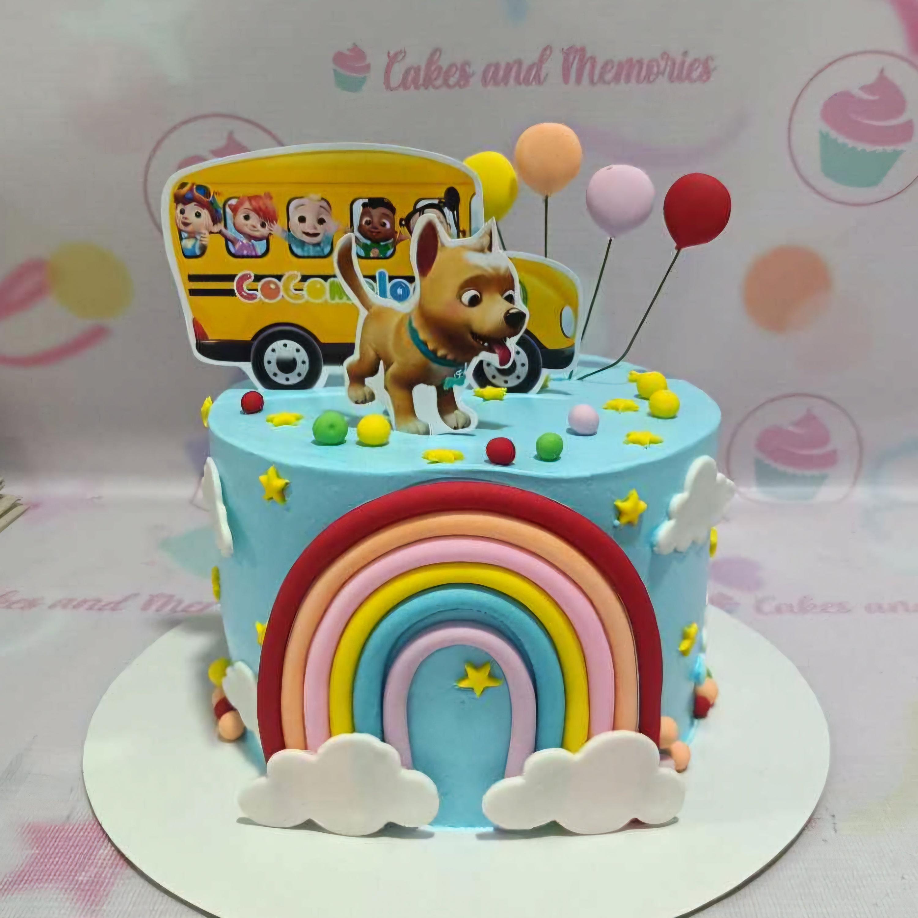 Light blue Cocomelon themed cake with a large fondant rainbow, white clouds, and printed character bus and dog toppers.