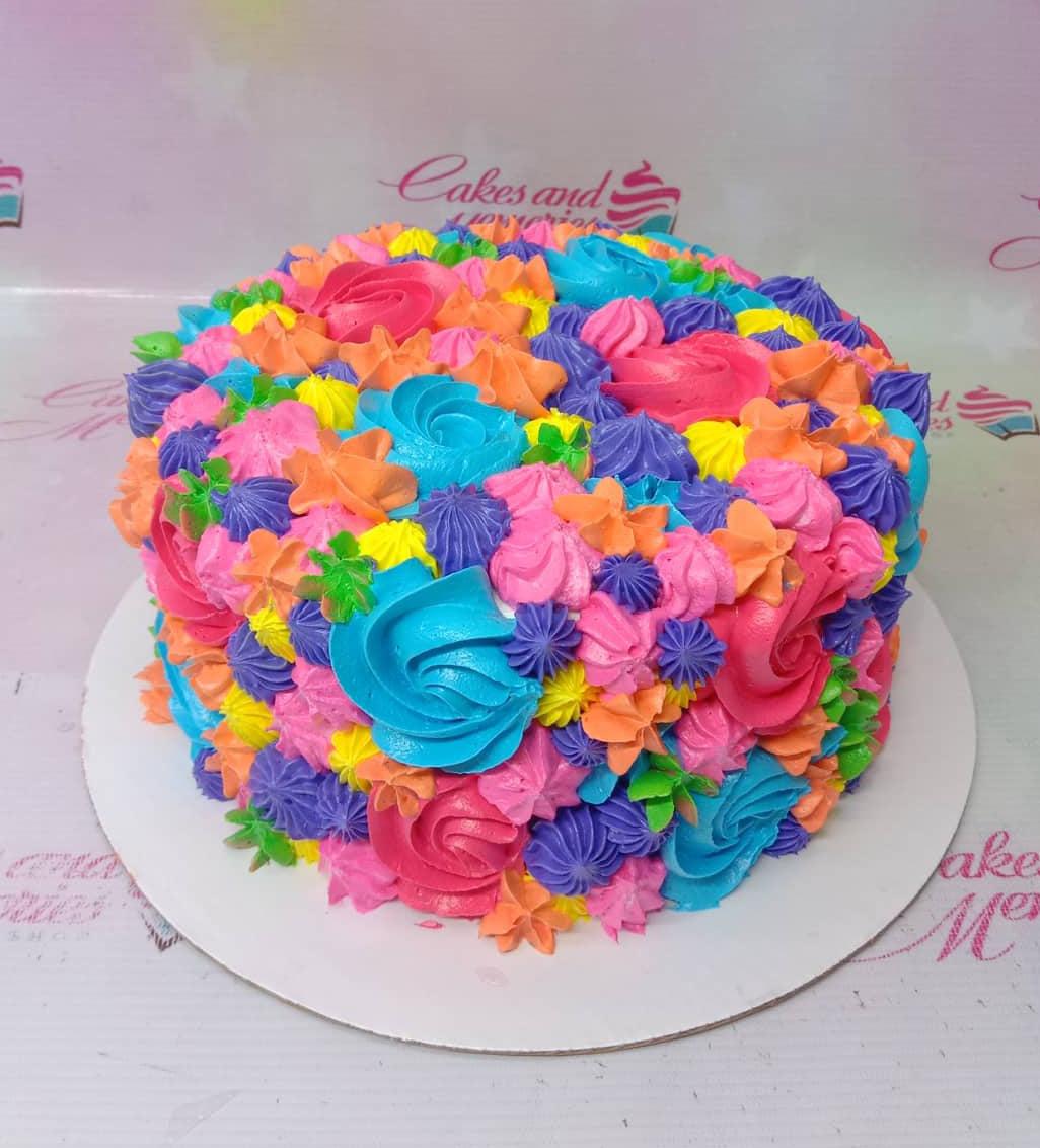 Vibrant multi-colored floral cake with intricate icing rosettes in pink, blue, orange, purple, and yellow.