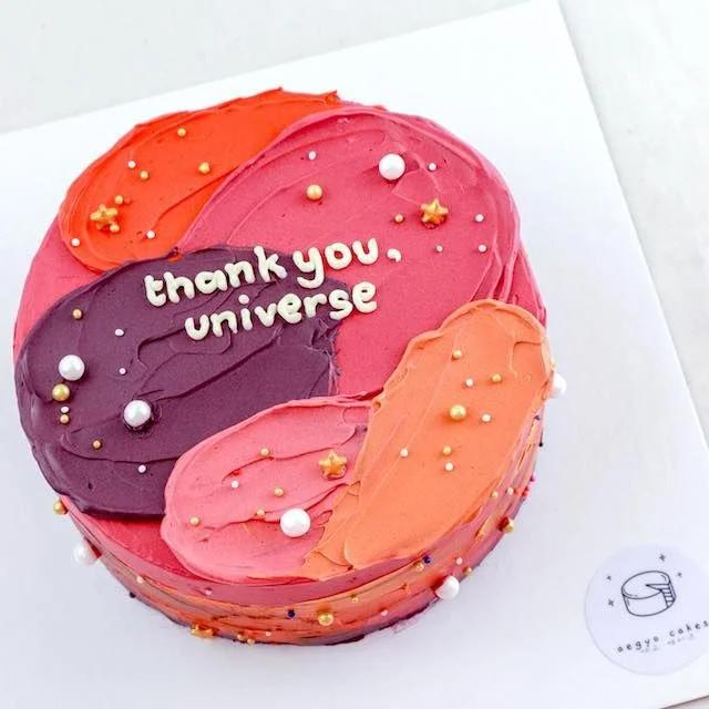 A colorful bento cake with a palette knife icing design in shades of pink, orange, and purple, decorated with pearls and gold stars.