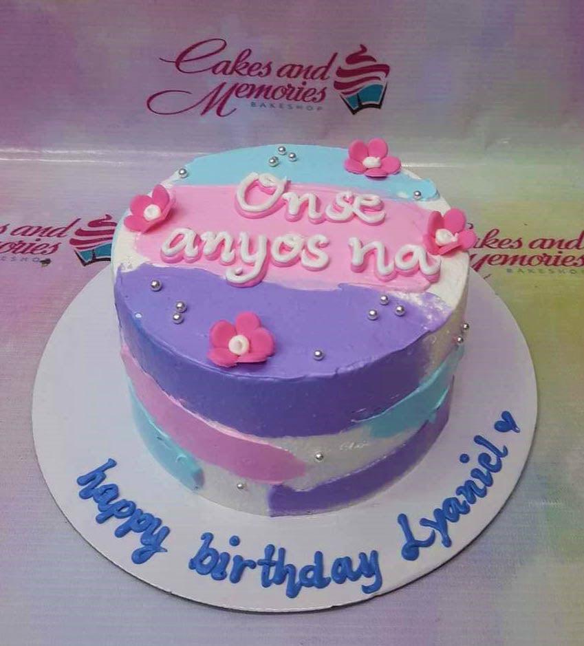 A colorful 1-tier birthday cake with pink, blue, and purple textured icing, pink fondant flowers, and silver dragees.
