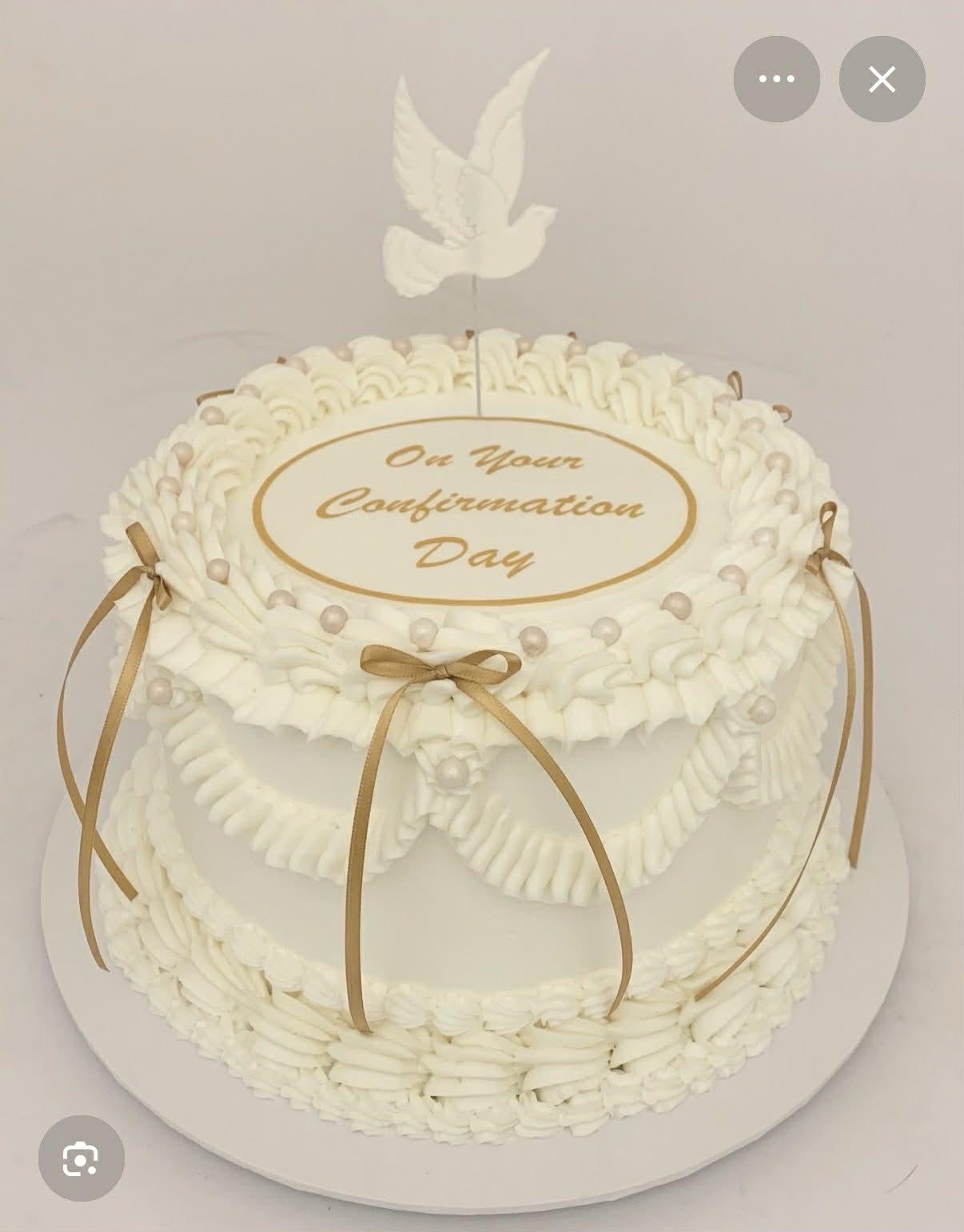 Elegant white vintage-style confirmation cake with piped ruffles, gold ribbons, and a white dove topper.