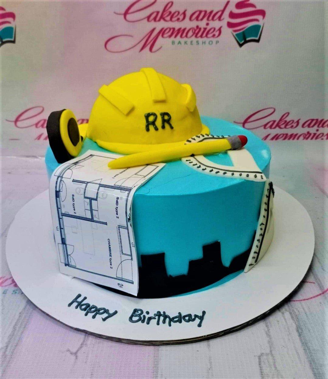 Light blue construction themed birthday cake with a yellow hard hat, blueprint printout, and architectural tools.