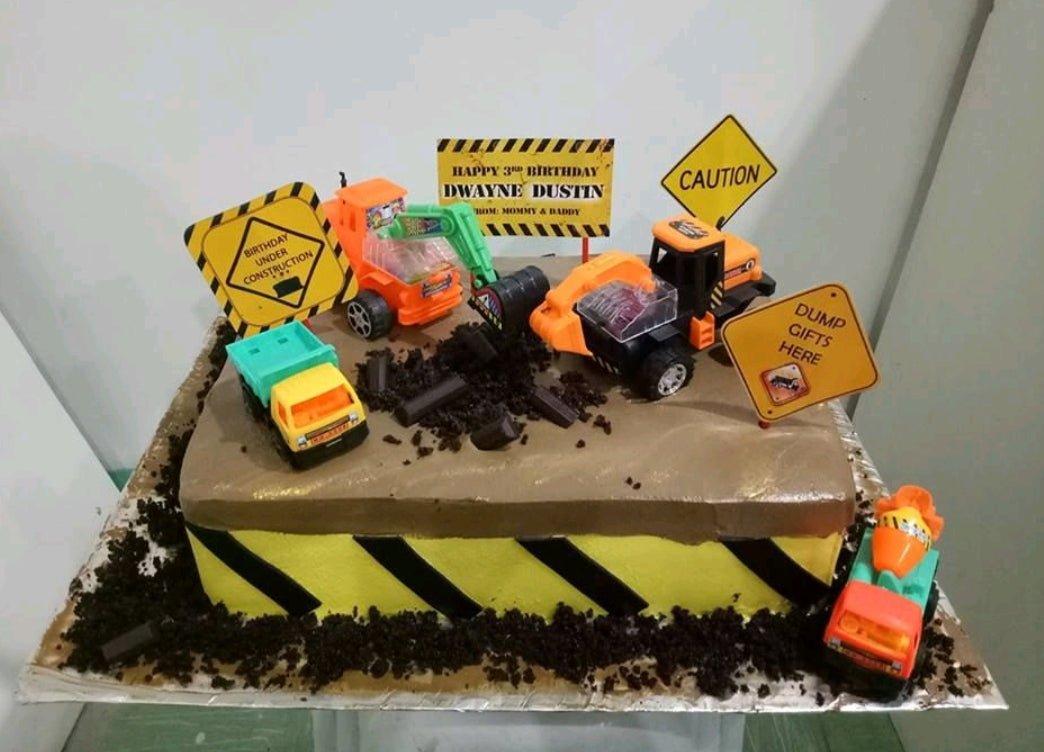 Construction themed rectangle cake with yellow and black hazard stripes, brown icing, and toy construction vehicles like excavators and dump trucks.