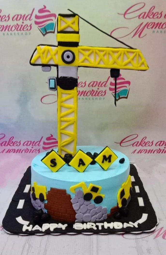 Light blue construction themed birthday cake with a large yellow crane topper and fondant construction vehicles.