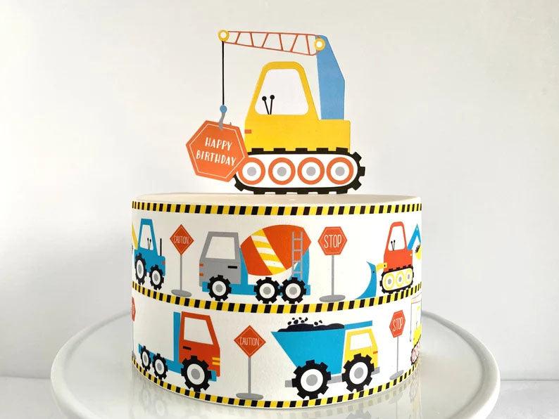 Construction themed birthday cake with a large yellow crane topper and colorful truck side wraps on white icing.