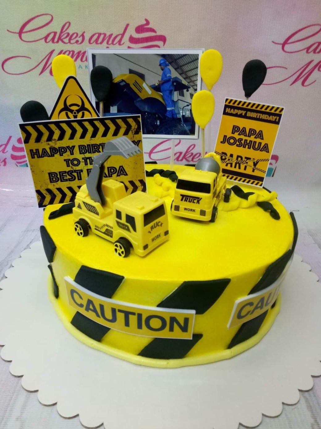 Yellow construction themed birthday cake with toy trucks, caution signs, and a photo topper for Papa Joshua.