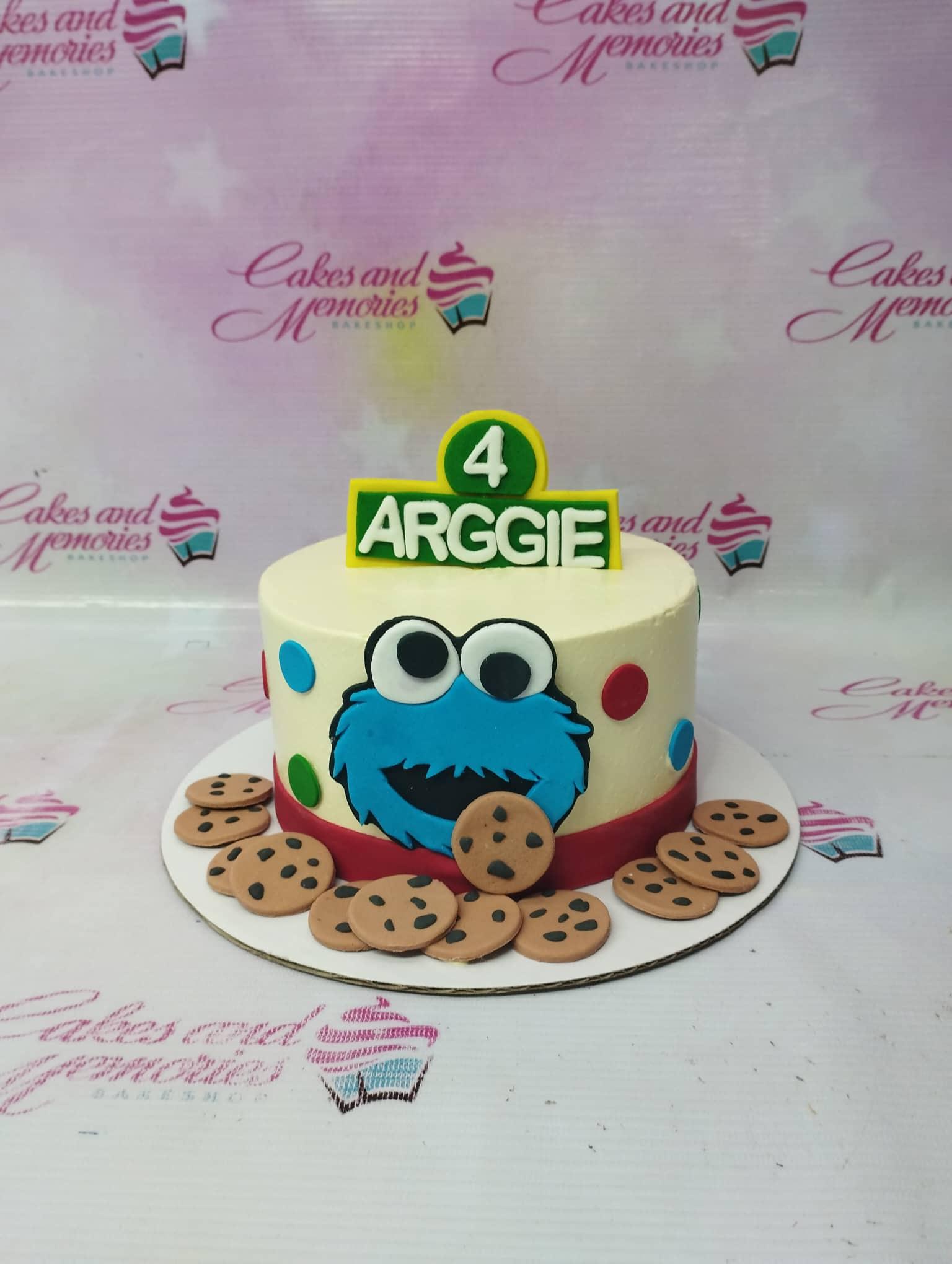 Cookie Monster themed birthday cake with blue fondant face, edible cookies, and a green name topper for Arggie's 4th birthday.