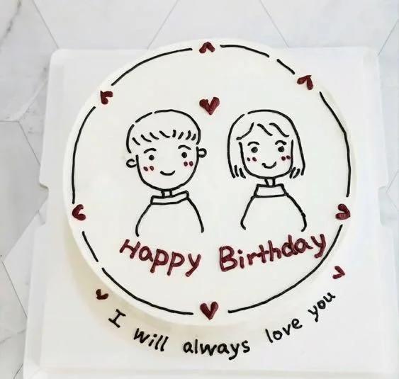 White bento cake with hand-drawn icing doodle of a couple, red hearts, and Happy Birthday message.