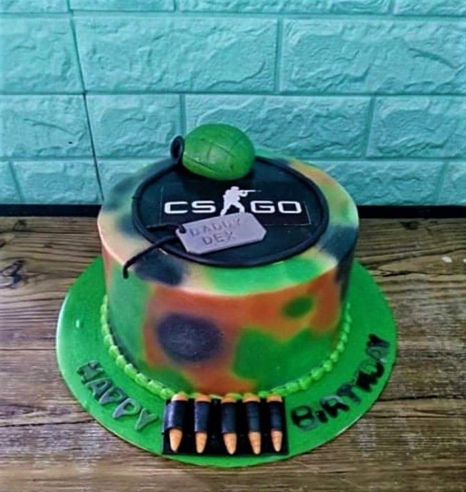 CSGO themed camouflage cake with a green grenade topper, dog tag, and bullet decorations on a green base board.