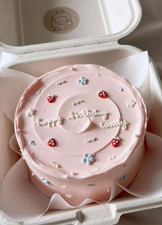 Pink bento cake with white icing text, piped flowers, and strawberry decorations in a clamshell box.