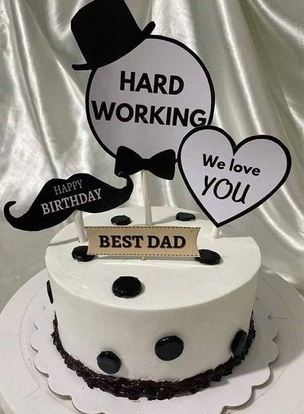 White minimalist cake for dad with black polka dots and various paper toppers including a top hat, mustache, and heart.