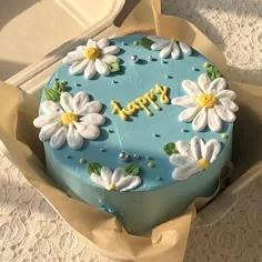 Light blue bento cake decorated with white piped icing daisies and a yellow 'happy' message in the center.
