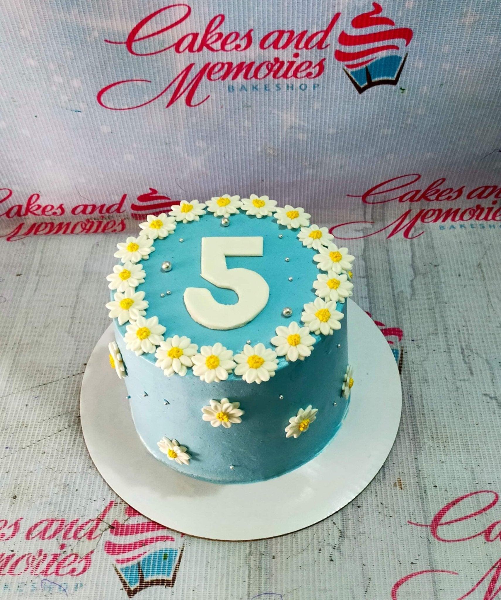Light blue birthday cake decorated with white and yellow fondant daisies and a large white number 5 topper.