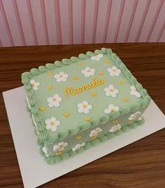 Light green rectangular cake with white icing daisies and yellow centers, featuring a yellow piped name message and green ruffled borders.