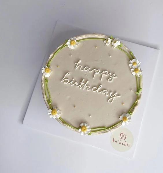 Minimalist beige bento cake with white piped daisy flowers and 'happy birthday' message in white icing.