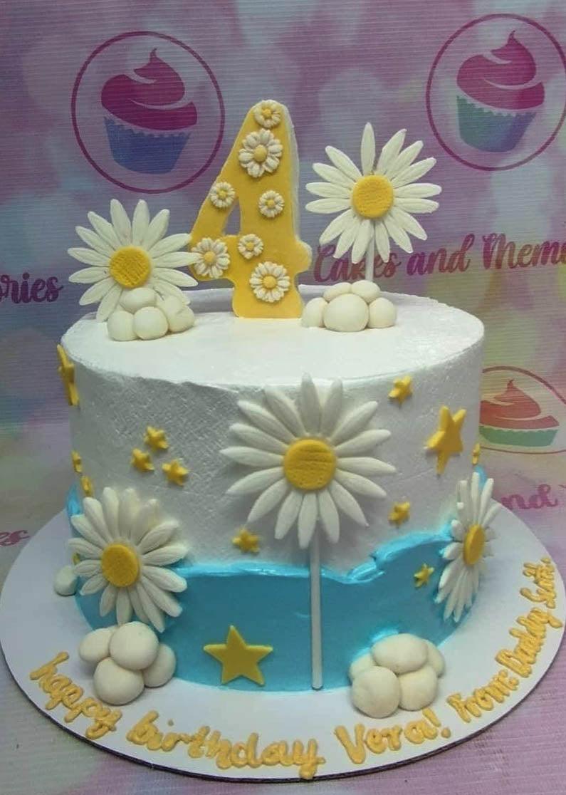 White and light blue birthday cake with yellow number 4 topper, white daisies, and yellow stars.