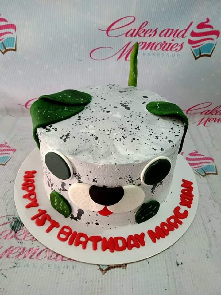 Dalmatian dog face cake with white icing, black spots, green fondant ears, and a red message on the base board.
