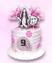 A light pink 1 tier cake featuring a Nezuko Kamado character, a cherry blossom tree backdrop, and a 'Demon Slayer' style logo with the name 'Dawn Jace', accented with pink fondant cherry blossoms and white pearl sprinkles.