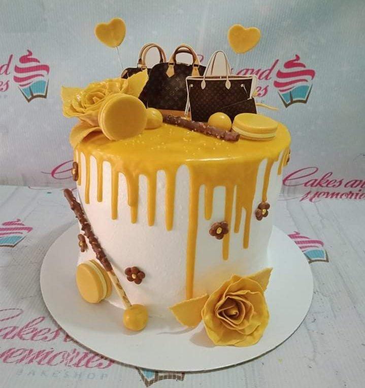 White 1-tier designer bag themed cake with yellow drip, yellow roses, macarons, and chocolate sticks.