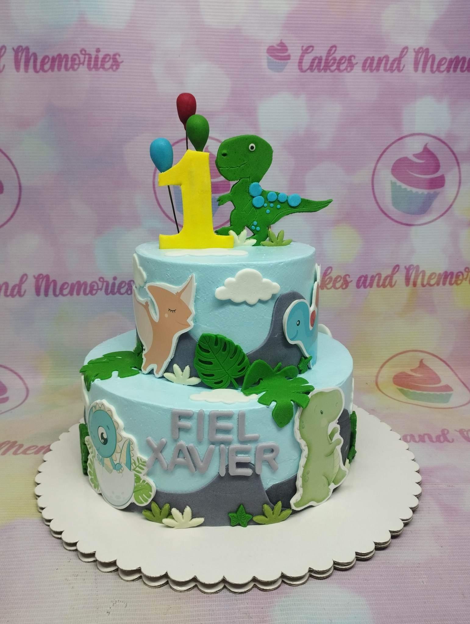 Two-tier light blue dinosaur themed birthday cake with fondant dinosaurs, clouds, and tropical leaves.
