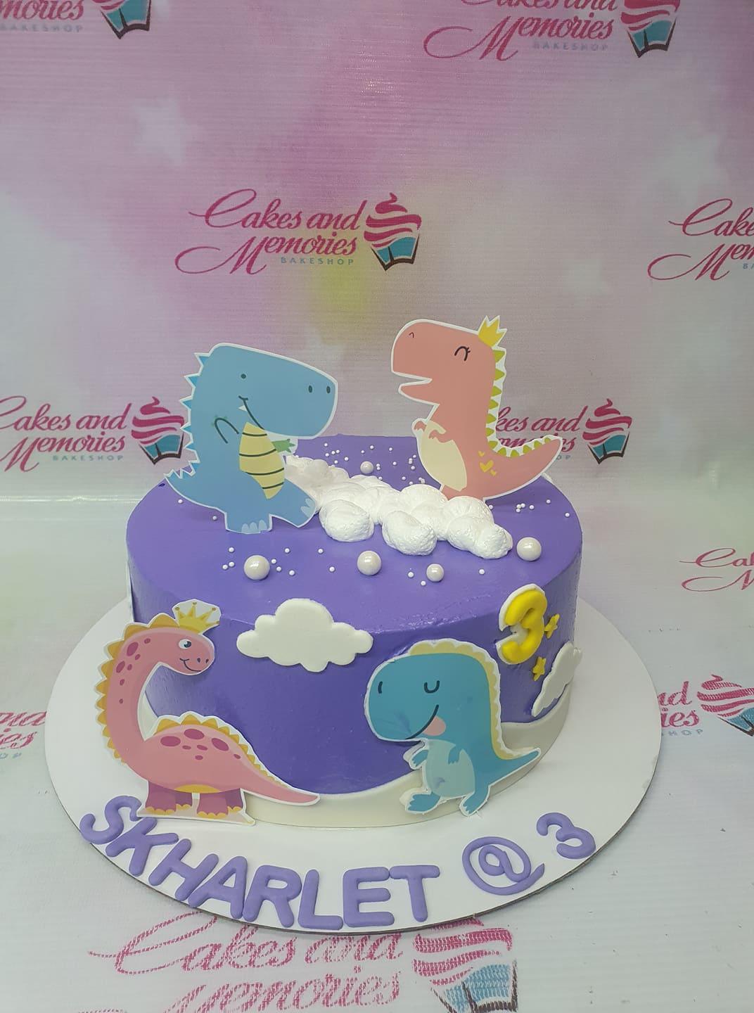 Purple dinosaur themed birthday cake with pink and blue dinosaur printouts, white fondant clouds, and pearls.