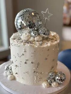 White textured buttercream cake decorated with various sized silver disco balls, silver stars, and white icing dollops.