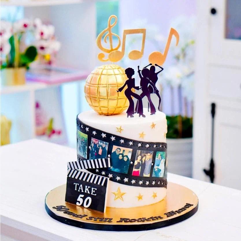 White 1-tier disco and movie themed cake with gold disco ball, music notes, dancing silhouettes, and a film strip with photos.