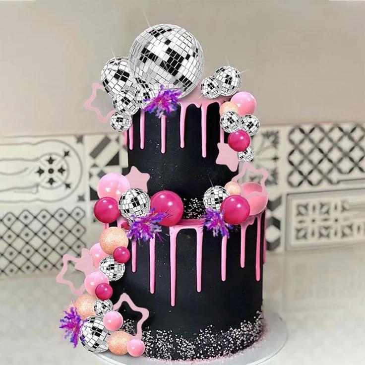 Two-tier black cake with pink drip, silver disco balls, pink balloons, and star accents.