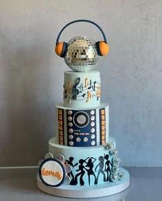 A three-tier light blue disco themed cake with a large disco ball topper wearing headphones, musical notes, and dancing silhouettes.