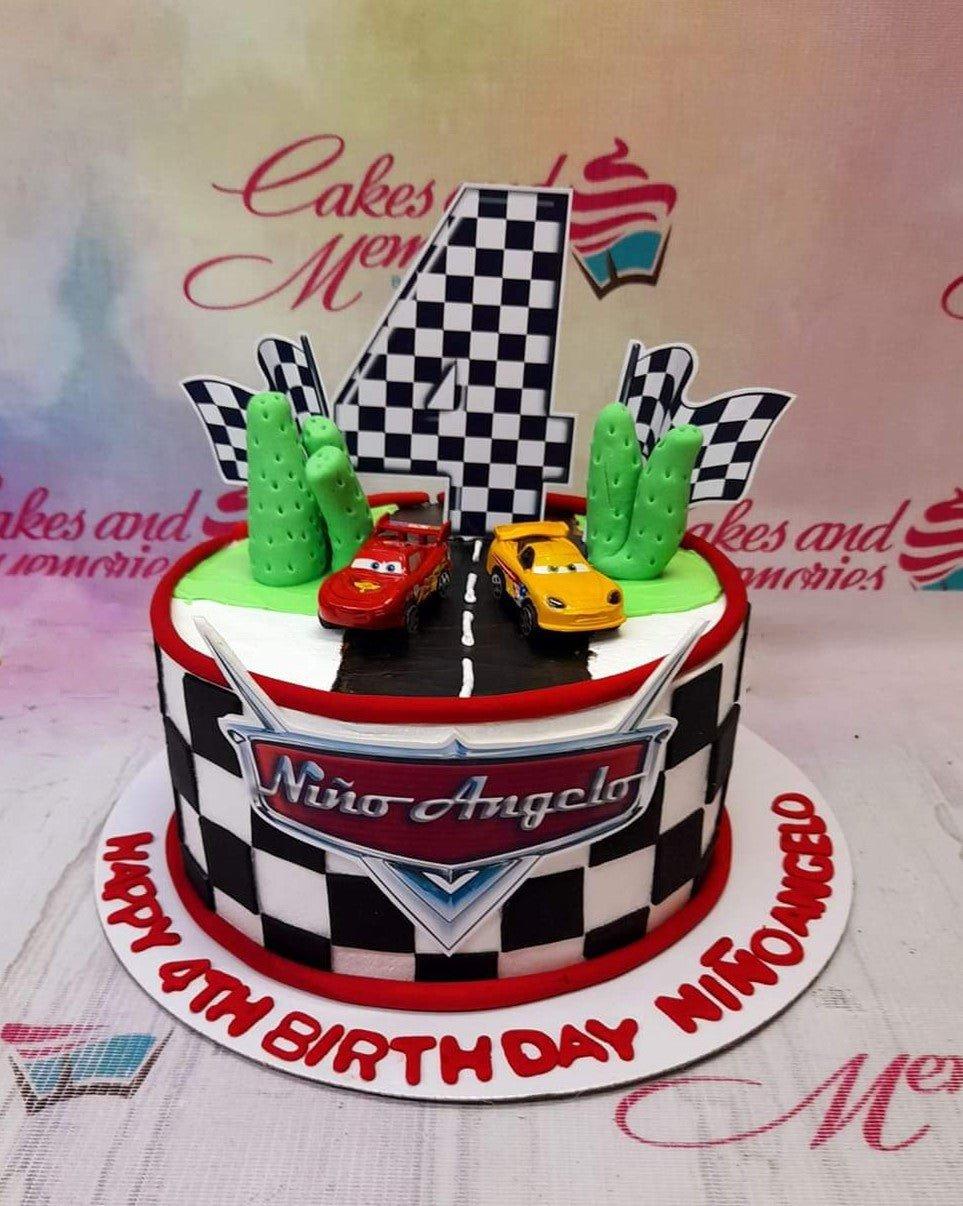 Disney Cars themed birthday cake with Lightning McQueen and Jackson Storm toy cars on a checkered racing track design.