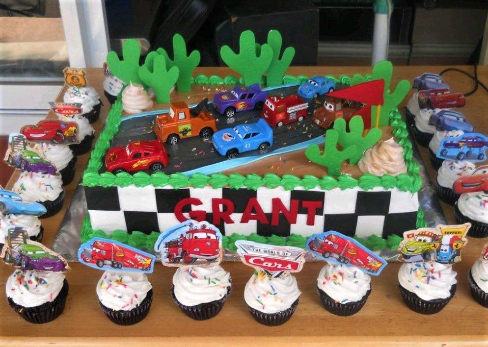 Disney Cars themed rectangle cake with toy cars, green cactus toppers, and a checkered flag side design for Grant's birthday.